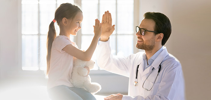 Young female patient holding a stuffed animal gives an "air" high-five to male doctor wearing lab coat and stethoscope