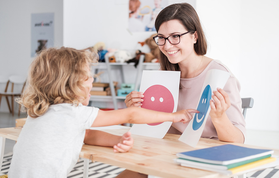 Young professional woman shows emotion drawings to a young child who points to one